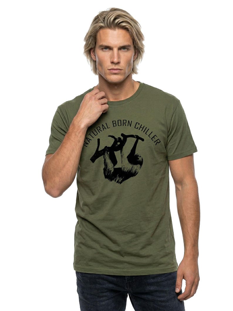 Pu&ograve; includere: T-shirt verde oliva con la scritta "NATURAL BORN CHILLER" sopra una grafica nera di un bradipo appeso a un ramo. La maglietta a maniche corte &egrave; realizzata in un materiale morbido.