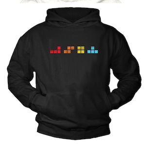 Pode incluir: Camisola de capuz preta com um design pixelado arco-íris na frente. O design é uma linha de cinco blocos pixelados de diferentes cores, que se assemelha a um videojogo.