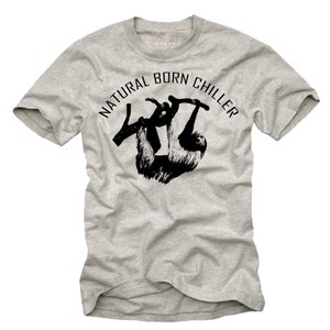 Pu&ograve; includere: T-shirt grigio chiaro con la scritta "NATURAL BORN CHILLER" in una forma curva sopra una silhouette nera di un bradipo appeso a un ramo. La maglietta ha maniche corte e girocollo.