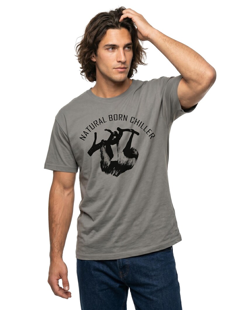 Pu&ograve; includere: T-shirt grigio con la scritta "NATURAL BORN CHILLER" e una grafica di bradipo nero. La maglietta &egrave; a girocollo e maniche corte. Il modello indossa jeans blu.
