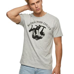 Pu&ograve; includere: T-shirt grigio chiaro con la scritta "NATURAL BORN CHILLER" e una grafica di bradipo nero. La maglietta &egrave; a maniche corte e ha un girocollo. Il modello indossa jeans azzurri.