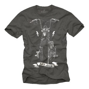 Puede incluir: Camiseta gris oscuro con un gr&aacute;fico plateado de motocicleta. El dise&ntilde;o incluye una vista frontal de la motocicleta, rayos y una pancarta con el texto "BAD SEED". La camiseta tiene mangas cortas y cuello redondo.