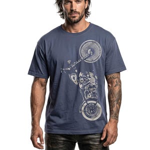 以下が含まれることがあります： ネイビーブルーのTシャツ。銀色のオートバイのグラフィックが特徴です。デザインは、前輪、エンジン、その他のオートバイの部品を示しています。Tシャツは無地で、クルーネックです。