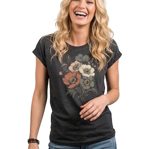 May include: Dark gray t-shirt featuring a floral design with orange, white, and gray flowers. The short-sleeved tee is paired with blue jeans. A brown leather bracelet is worn on the left wrist.