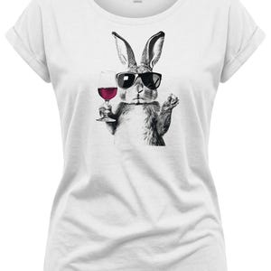 May include: White t-shirt featuring a black and white illustration of a rabbit wearing sunglasses and holding a glass of red wine. The rabbit is depicted in a relaxed pose, suggesting a casual and fun vibe. The shirt has rolled-up sleeves.