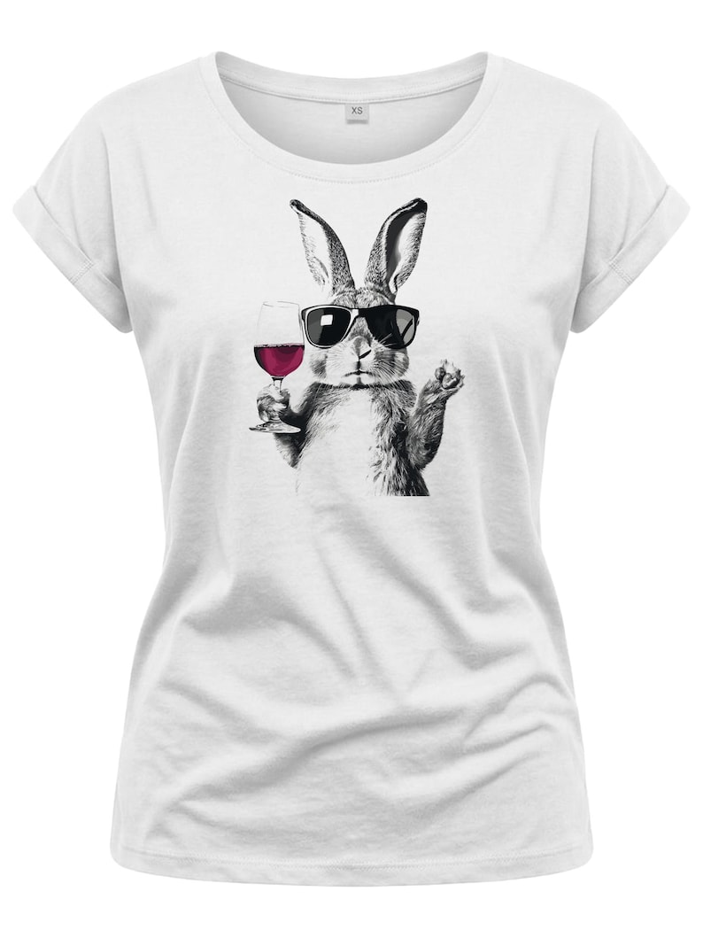 May include: White t-shirt featuring a black and white illustration of a rabbit wearing sunglasses and holding a glass of red wine. The rabbit is depicted in a relaxed pose, suggesting a casual and fun vibe. The shirt has rolled-up sleeves.