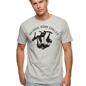 Pu&ograve; includere: T-shirt grigio chiaro con la scritta "NATURAL BORN CHILLER" sopra una grafica nera di un bradipo appeso a un ramo. La maglietta ha maniche corte e girocollo.