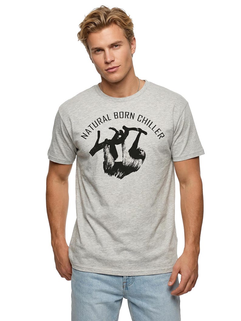 Pu&ograve; includere: T-shirt grigio chiaro con la scritta "NATURAL BORN CHILLER" sopra una grafica nera di un bradipo appeso a un ramo. La maglietta ha maniche corte e girocollo.