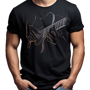 May include: Black t-shirt featuring a line art illustration of hands playing a guitar. The guitar strings and hands are outlined in orange and white against the black fabric. The model is wearing blue jeans.