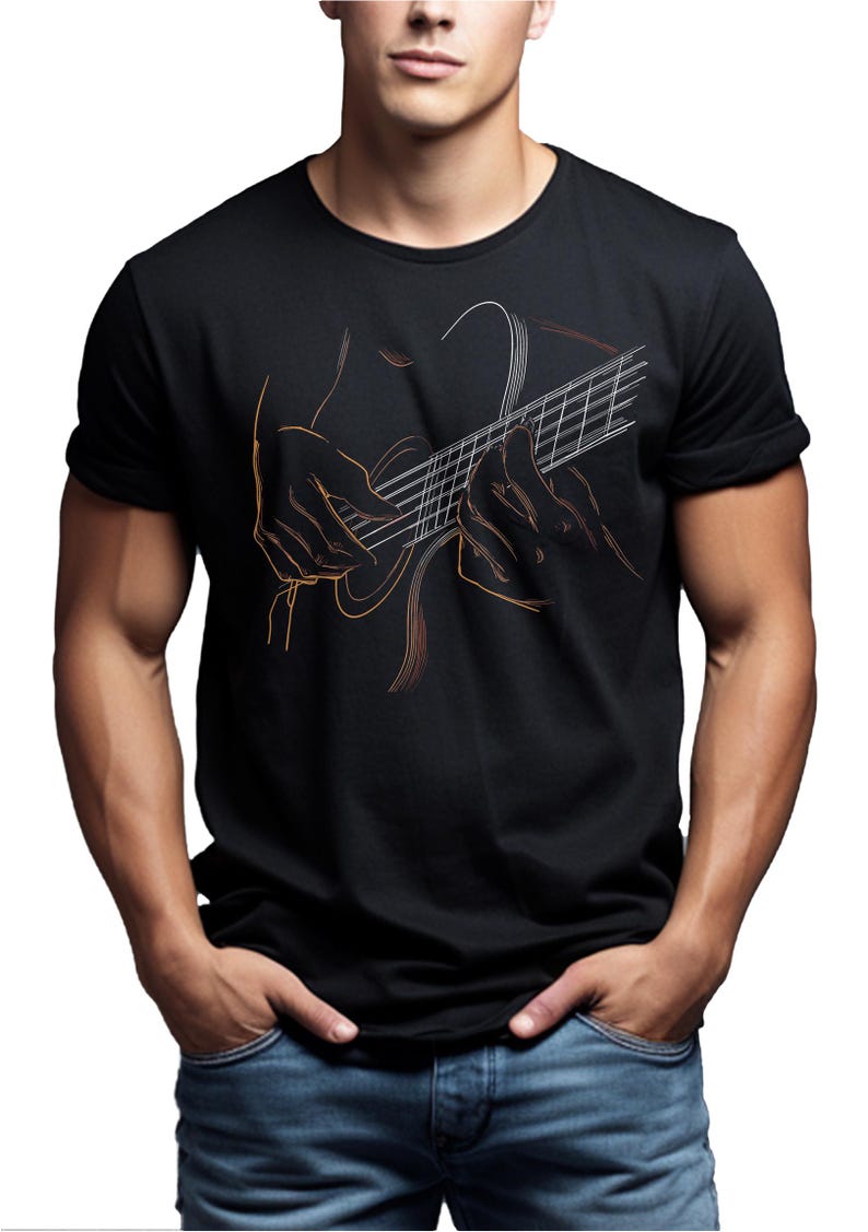 May include: Black t-shirt featuring a line art illustration of hands playing a guitar. The guitar strings and hands are outlined in orange and white against the black fabric. The model is wearing blue jeans.