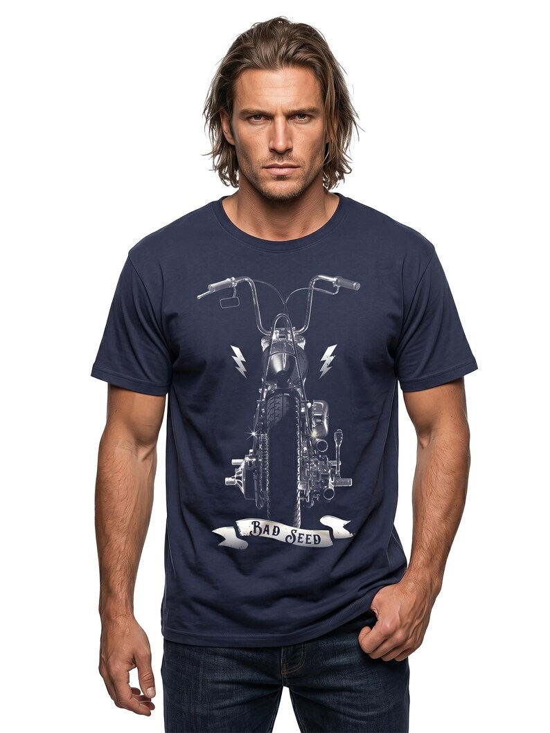 Puede incluir: Camiseta azul marino con una ilustraci&oacute;n detallada en escala de grises de la parte delantera de una motocicleta. El dise&ntilde;o incluye rayos y una pancarta que dice "BAD SEED". La camiseta la lleva una persona con pelo largo y casta&ntilde;o claro.