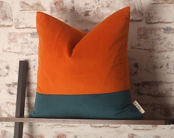 May include: A decorative pillow with a two-tone design. The top half is a vibrant orange velvet, and the bottom half is a deep teal velvet. The pillow has a small tag with the text "My Cozy" on it.
