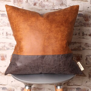 May include: A brown and gray faux leather pillow with a brown top and a gray bottom. The pillow is sitting on a silver stool.