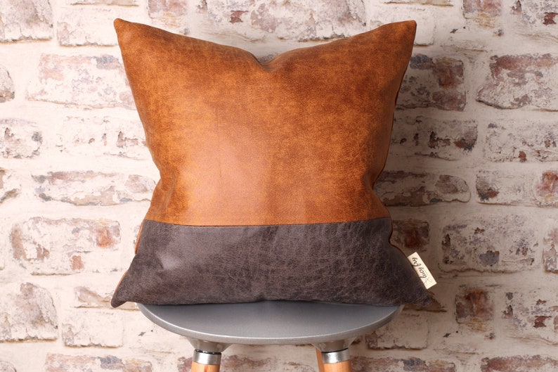May include: A brown and gray faux leather pillow with a brown top and a gray bottom. The pillow is sitting on a silver stool.