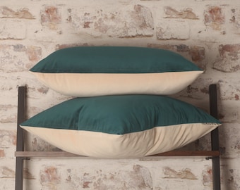May include: Two decorative pillows with a teal green velvet front and a cream colored back. The pillows are stacked on top of each other on a wooden shelf.