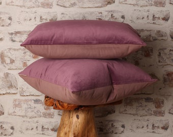 May include: Two mauve velvet throw pillows with a light pink underside. The pillows are stacked on top of each other and are sitting on a wooden stump.