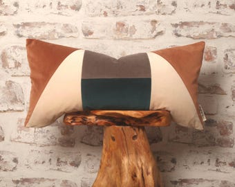 May include: A geometric patterned throw pillow with brown, beige, gray, and teal velvet fabric. The pillow is sitting on a wooden stool.