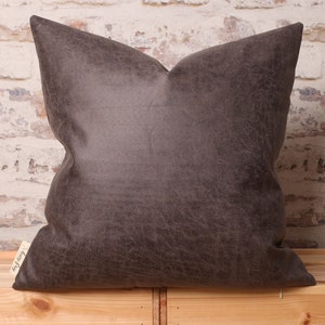May include: A dark brown faux leather pillow with a subtle textured surface. The pillow is square and has a simple design.