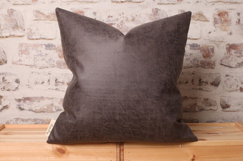May include: A dark brown faux leather pillow with a subtle textured surface. The pillow is square and has a simple design.
