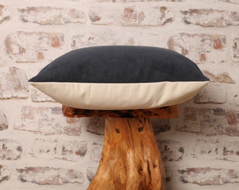 May include: A dark gray corduroy pillow with a cream colored border. The pillow is sitting on a wooden stump.