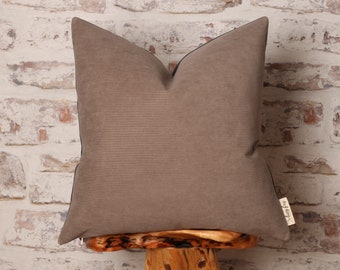 May include: A brown corduroy pillow with a black trim and a small white label with the text "My Cozy" on it. The pillow is sitting on a wooden stool.