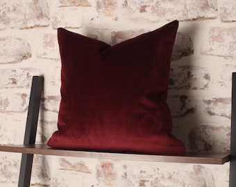 May include: A deep red velvet pillow on a wooden shelf. The pillow is square and has a smooth, soft texture.