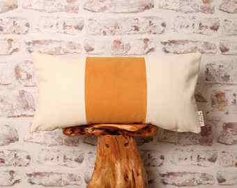May include: A white and mustard yellow lumbar pillow with a corduroy texture. The pillow is sitting on a wooden stool.