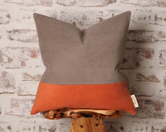 May include: A brown and orange corduroy pillow with a brown and white label that says "The Cozy Nest".
