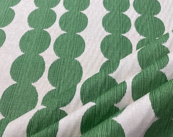 May include: A white fabric with a repeating pattern of green circles. The circles are arranged in vertical rows, with each row offset from the one above it. The fabric is folded in half, with the fold line running diagonally across the image.