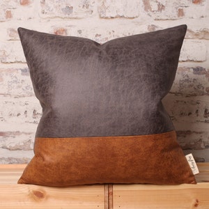 May include: A brown and gray throw pillow with a distressed leather look. The pillow has a brown bottom half and a gray top half.