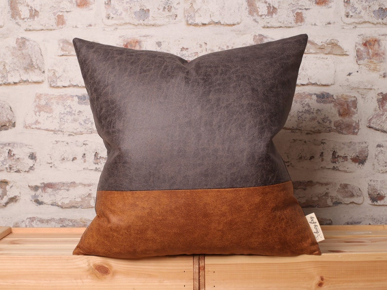 May include: A brown and gray throw pillow with a distressed leather look. The pillow has a brown bottom half and a gray top half.