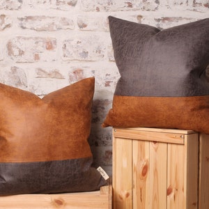 May include: Two decorative throw pillows with a brown and gray faux leather design. The pillows are on wooden crates.
