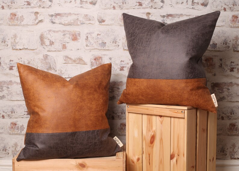 May include: Two decorative throw pillows with a brown and gray faux leather design. The pillows are on wooden crates.