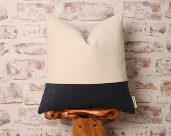 May include: A white and dark gray pillow with a textured fabric. The pillow is sitting on a wooden stool.