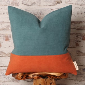 May include: Teal and orange corduroy cushion with a contrasting colour block design. The cushion is sitting on a wooden stool.