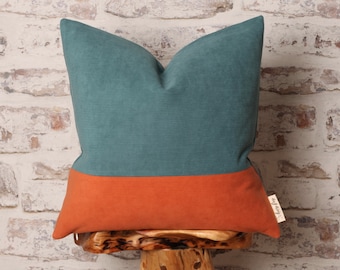 May include: Teal and orange corduroy pillow with a contrasting color block design. The pillow is sitting on a wooden stool.