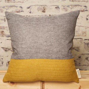 Pode incluir: Travesseiro decorativo cinza e amarelo com tecido texturizado. O travesseiro tem a metade superior cinza e a metade inferior amarela. O travesseiro tem uma etiqueta que diz "my cozy".
