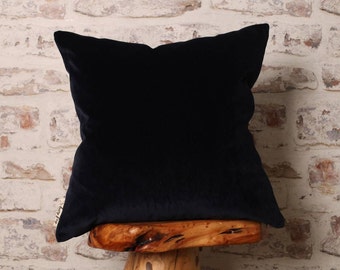 May include: A dark blue velvet pillow with a plain design. The pillow is sitting on a wooden stool.