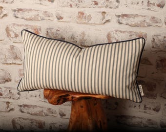 May include: Rectangular decorative pillow with a cream-colored background and vertical navy blue stripes. The pillow has a navy blue border and is placed on a wooden stand against a brick wall. The pillow has a tag that says "dotty dog".