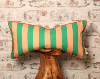 May include: A green and peach striped throw pillow with a coral trim. The pillow is sitting on a wooden stand.
