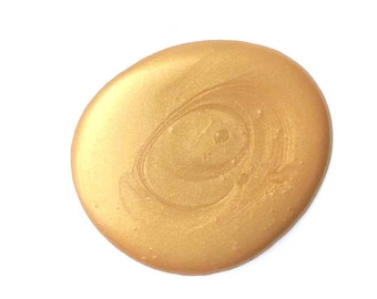 Può includere: Una macchia circolare di vernice dorata metallizzata con una finitura liscia e lucida. La superficie mostra sottili motivi a vortice e variazioni nel riflesso della luce, creando un aspetto ricco e scintillante su tutta la forma.