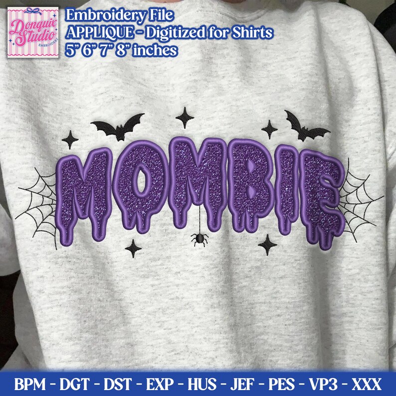 May include: A light gray sweatshirt featuring a purple glittery applique design that spells the word MOMBIE in a dripping font. The design includes black embroidered spiderwebs, bats, stars, and a small spider, available in 5, 6, 7, and 8 inches.