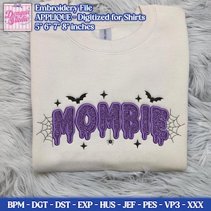 May include: A cream-colored crewneck sweatshirt featuring a purple glittery embroidered design that reads MOMBIE in a dripping font. The design includes black embroidered bats, spiderwebs, stars, and a small spider. Text at the top reads Embroidery File APPLIQUE - Digitized for Shirts 5 6 7 8 inches.