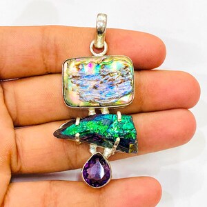 Può includere: Ciondolo in argento con conchiglia di abalone rettangolare, pietra iridescente verde e nera e ametista viola a forma di goccia. Il ciondolo ha un'ansa in argento per una collana.