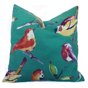 May include: Teal pillow with a watercolor bird pattern. The birds are painted in shades of red, orange, yellow, blue, and purple. The pillow is made of a soft, textured fabric.