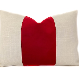May include: A white pillow with a red velvet stripe down the center. The pillow is made of a soft, textured fabric.