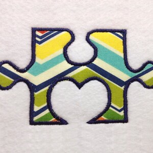 May include: A blue, green, yellow, and white chevron patterned puzzle piece with a heart-shaped cutout in the center.