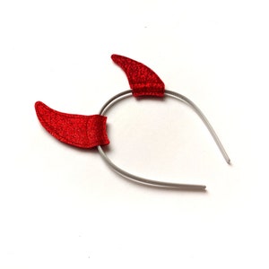 以下が含まれることがあります： 赤いグリッターの悪魔の角のヘッドバンドと銀色のプラスチックのヘッドバンド