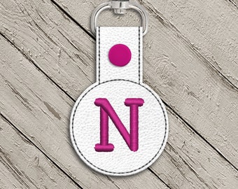 May include: White leather keychain with a pink circle and the letter N embroidered in pink.