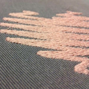 May include: A close-up of a grey fabric with a pink embroidered heart design.